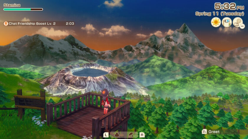 A screenshot from Story of Seasons: Grand Bazaar shows the female protagonist standing on a wooden viewing platform overlooking a stunning mountain landscape at sunset. In the distance, a crater lake sits nestled among snow-capped peaks and rolling green hills. The foreground features a dense forest of pine trees, and the sky glows with warm orange and purple hues. The interface shows the time as 5:32 PM on Spring 11 (Tuesday), with a notification for “Chat Friendship Boost Lv. 2.” The scene captures a moment of quiet reflection and natural beauty. Published on: LadiesGamers.